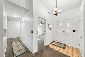 Entryway with light carpet, light tile patterned floors, a textured ceiling, a chandelier, and lofted ceiling