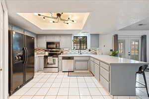 Kitchen with black appliances, a peninsula, decorative backsplash, light countertops, and a textured ceiling