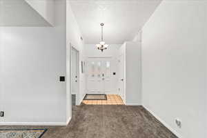 Foyer with light carpet, a textured ceiling, a chandelier, and light tile patterned floors