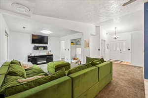 Living area with carpet, a textured ceiling, a ceiling fan, and a chandelier