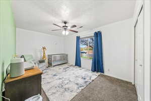 Carpeted bedroom featuring a crib, a textured ceiling, a ceiling fan, and a closet