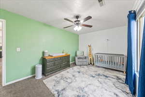 Carpeted bedroom featuring a crib, a textured ceiling, and ceiling fan