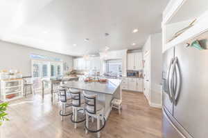 Kitchen with appliances with stainless steel finishes, a kitchen island, white cabinetry, hanging light fixtures, and light wood-type flooring