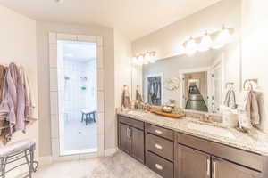 Full bath with double vanity, tiled shower, and light tile patterned floors