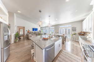 Kitchen with white cabinets, stainless steel appliances, open floor plan, light wood-style floors, and an island with sink