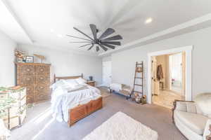Carpeted bedroom featuring a raised ceiling, ceiling fan, recessed lighting, and ensuite bathroom