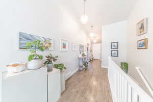 Hall featuring light wood-style flooring, high vaulted ceiling, and an upstairs landing