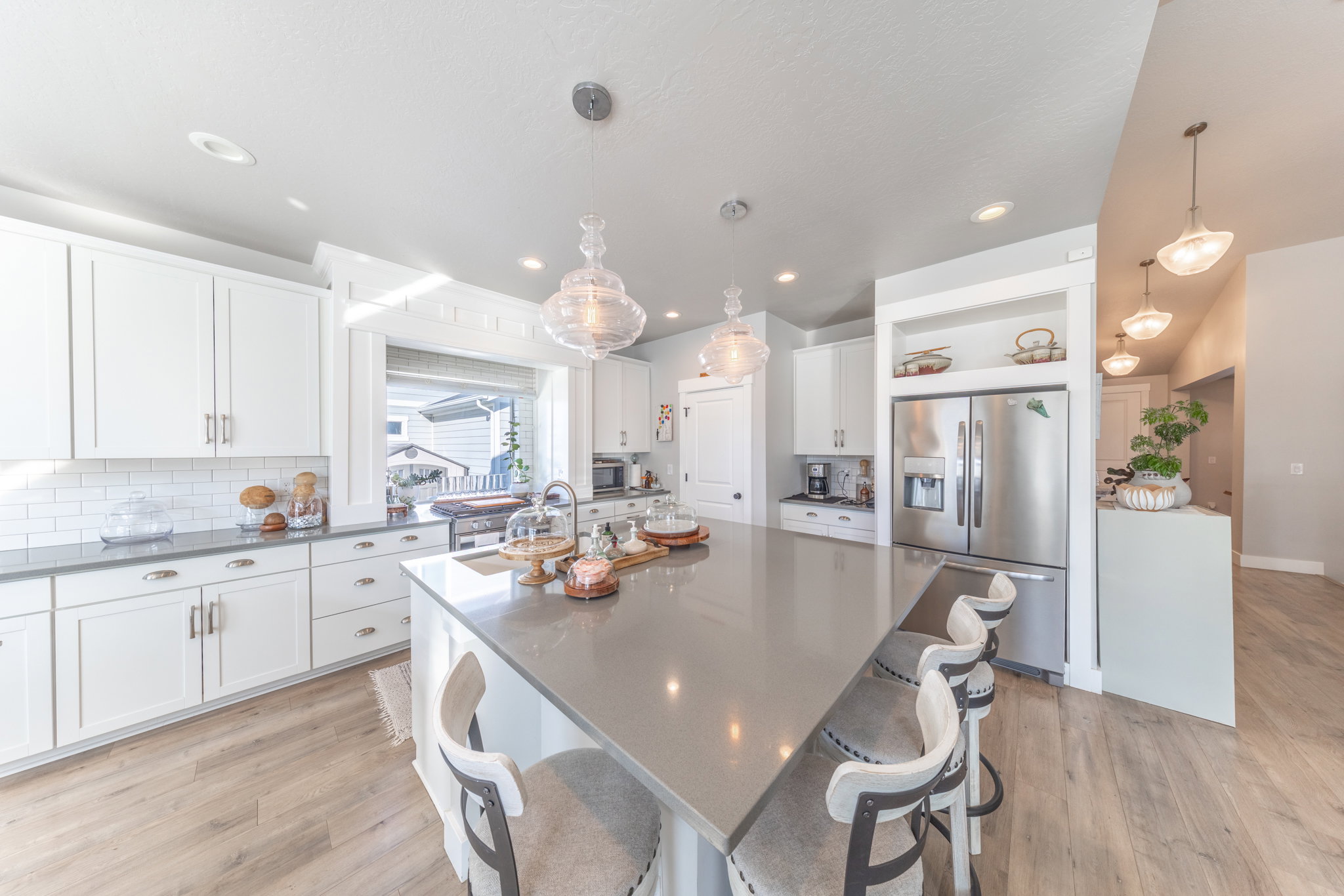 Kitchen with tasteful backsplash, stainless steel fridge, light wood-style flooring, white cabinetry, and a kitchen island with sink
