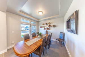 Carpeted dining space featuring a raised ceiling and baseboards