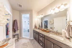 Bathroom featuring a walk in closet, double vanity, light tile patterned floors, and a walk in shower