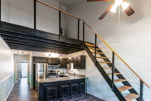 Kitchen with dark wood-style floors, appliances with stainless steel finishes, a kitchen bar, light stone counters, and a towering ceiling