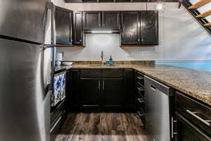 Kitchen with appliances with stainless steel finishes, dark wood finished floors, dark stone counters, and dark cabinetry