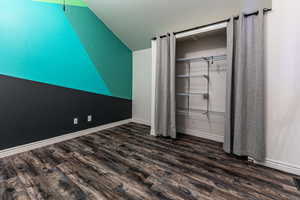 Unfurnished bedroom featuring dark wood-type flooring and vaulted ceiling