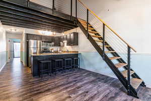 Kitchen with dark wood finished floors, a breakfast bar area, stainless steel appliances, light stone countertops, and a towering ceiling