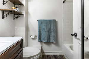 Full bath with dark wood finished floors, vanity, shower / bath combination, and a textured wall