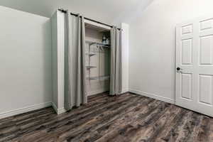 Unfurnished bedroom featuring dark wood finished floors, a closet, and vaulted ceiling