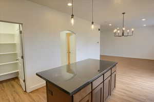 Kitchen featuring a center island, light wood-style flooring, arched walkways, hanging light fixtures, and recessed lighting