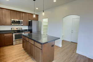Kitchen with stainless steel appliances, pendant lighting, arched walkways, a center island, and light wood-style flooring