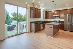 Kitchen with appliances with stainless steel finishes, light wood-style flooring, dark countertops, a chandelier, and a kitchen island