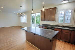 Kitchen featuring pendant lighting, a kitchen island, light wood finished floors, dark stone countertops, and brown cabinets