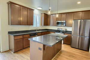Kitchen featuring appliances with stainless steel finishes, hanging light fixtures, a kitchen island, light wood finished floors, and brown cabinetry