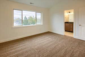 Master bedroom with light carpet, lofted ceiling, and ensuite bath
