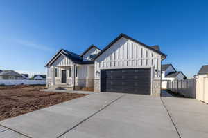 Modern farmhouse featuring board and batten siding, stone siding, concrete driveway, and an attached garage