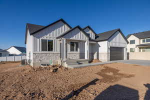 Modern inspired farmhouse with board and batten siding, concrete driveway, stone siding, a garage, and roof with shingles