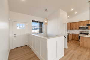 Kitchen featuring decorative backsplash, appliances with stainless steel finishes, recessed lighting, hanging light fixtures, and light wood-style flooring