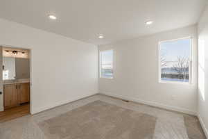 Primary bedroom with light carpet, recessed lighting, and ensuite bathroom