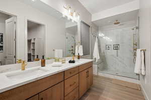 Full bathroom featuring double vanity, a marble finish shower, light wood finished floors, and a walk in closet