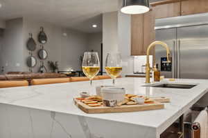 Kitchen featuring light stone counters, stainless steel built in refrigerator, a breakfast bar area, an island with sink, and decorative light fixtures