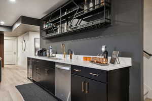 Bar area with dark cabinets, open shelves, light wood-style flooring, dishwasher, and light stone countertops