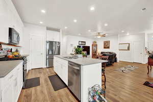 Kitchen featuring stainless steel appliances, white cabinetry, recessed lighting, a kitchen island with sink, quartz countertops, and light wood finished floors
