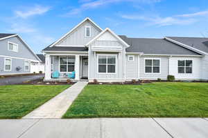 View of front of house with board and batten siding, roof with shingles, covered porch, and a front yard