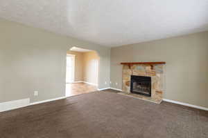 Unfurnished living room featuring a textured ceiling, dark carpet, arched walkways, and a stone fireplace