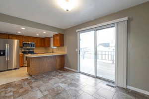 Kitchen with light countertops, stainless steel appliances, brown cabinets, recessed lighting, and light stone finish floors