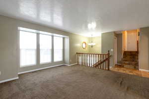 Carpeted empty room featuring a textured ceiling, a chandelier, and stairway