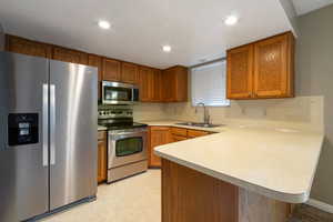 Kitchen featuring stainless steel appliances, brown cabinets, a peninsula, light countertops, and recessed lighting