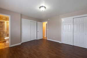 Unfurnished bedroom featuring two closets, dark wood-type flooring, ensuite bath, and a textured ceiling