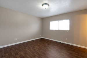 Empty room with a textured ceiling and dark wood-style flooring