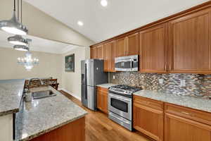 Kitchen with appliances with stainless steel finishes, brown cabinetry, pendant lighting, light wood-style floors, and light stone counters