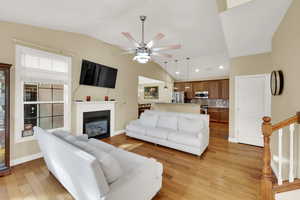 Living area featuring lofted ceiling, light wood finished floors, a glass covered fireplace, and a ceiling fan