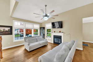 Living room featuring light wood-type flooring, a glass covered fireplace, ceiling fan, and lofted ceiling