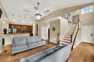 Living room with light wood-style flooring, stairway, high vaulted ceiling, and a ceiling fan