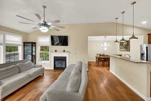 Living room featuring vaulted ceiling, light wood finished floors, a glass covered fireplace, and a ceiling fan