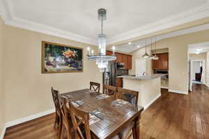Dining room with dark wood-type flooring, a chandelier, vaulted ceiling, and ornamental molding
