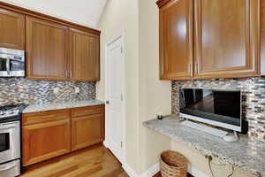 Kitchen with tasteful backsplash, appliances with stainless steel finishes, light stone countertops, and brown cabinets