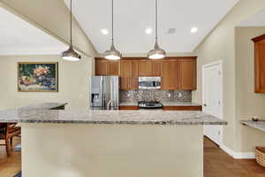 Kitchen with brown cabinets, appliances with stainless steel finishes, dark wood-type flooring, vaulted ceiling, and decorative backsplash