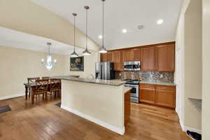 Kitchen featuring brown cabinets, light stone counters, pendant lighting, stainless steel appliances, and backsplash